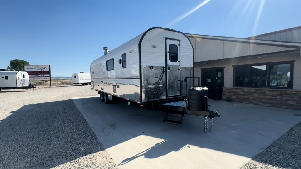 Front three-quarter view of the Kendall Camp with its raised front entry, steps, white siding, and diamond-plate lower panels.