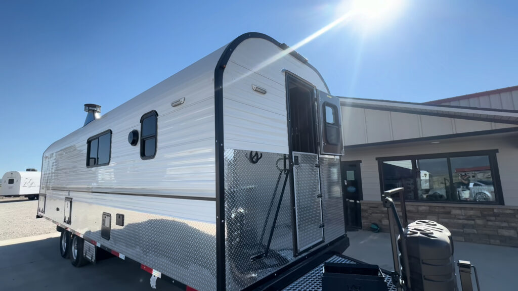 Low-angle exterior view of the Kendall Camp front entry, side windows, white siding, and diamond-plate lower panels.