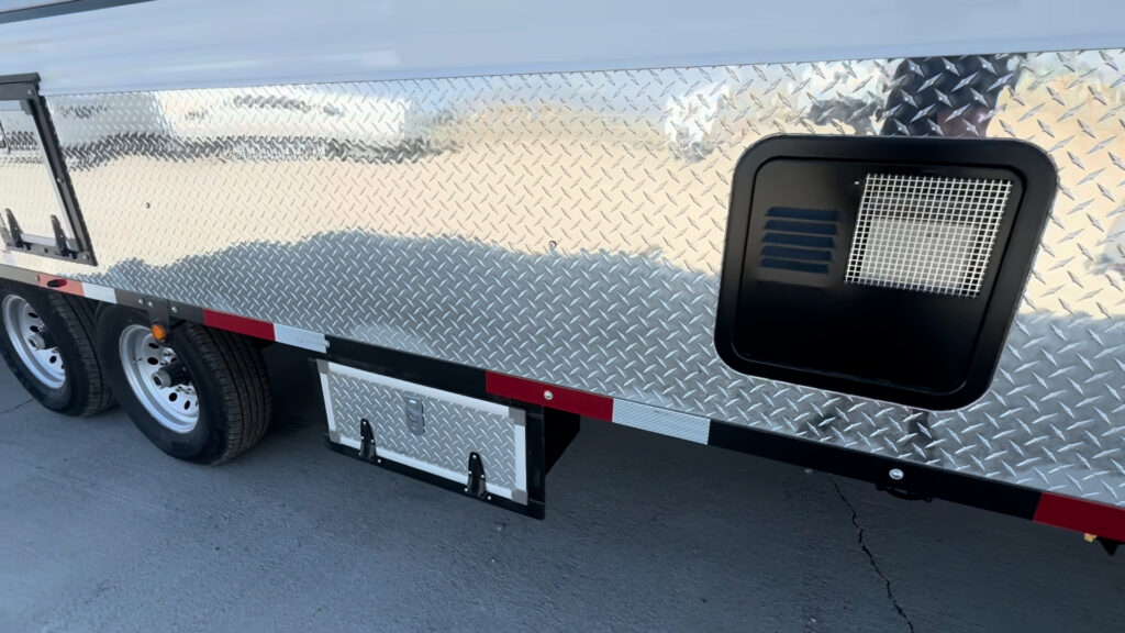 Side view of a Kendall Camp under-frame storage box below the diamond-plate lower panel and utility opening.