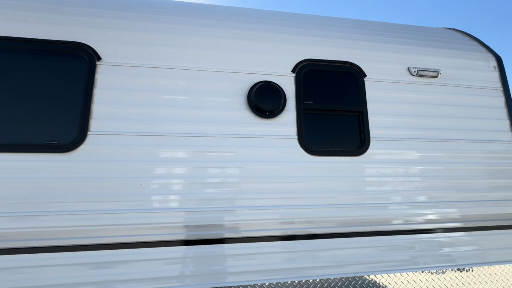 Close view of two Kendall Camp side windows and a round exterior vent in the white siding.