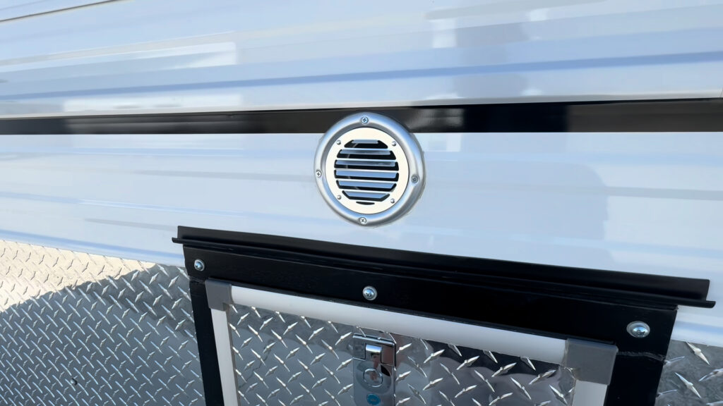 Round exterior vent above a latched diamond-plate access hatch on the Kendall Camp sidewall.