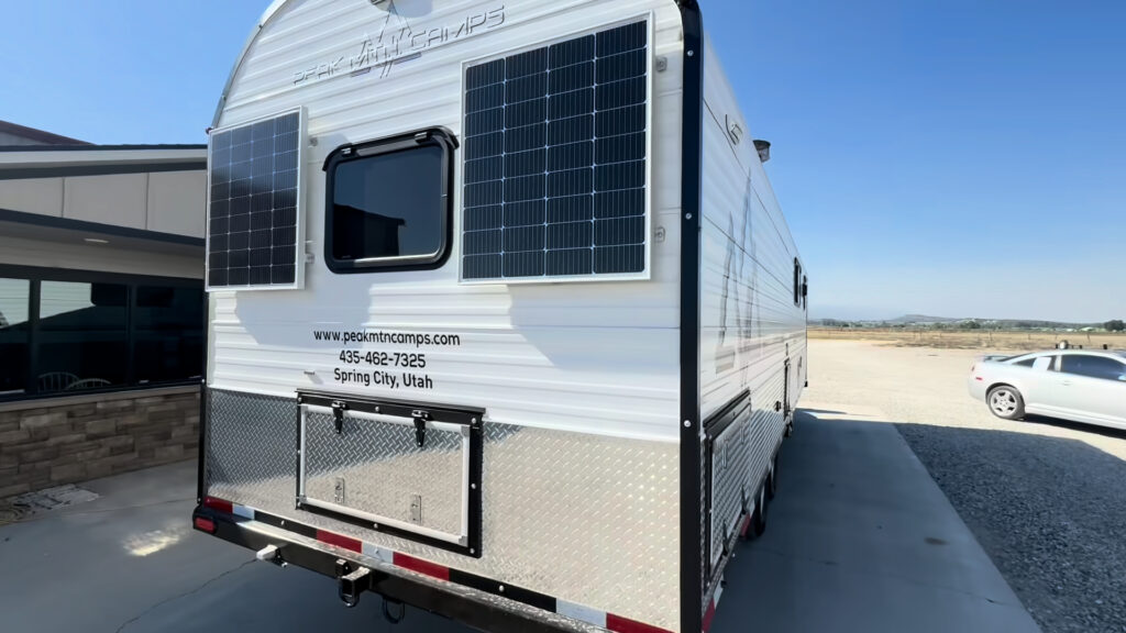 Rear three-quarter view of the Kendall Camp showing two wall-mounted solar panels, rear window, and lower access hatch.