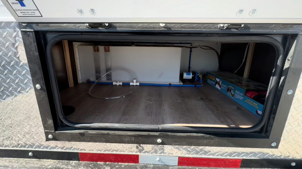 Open lower rear compartment on the Kendall Camp with visible plumbing and stored supplies.