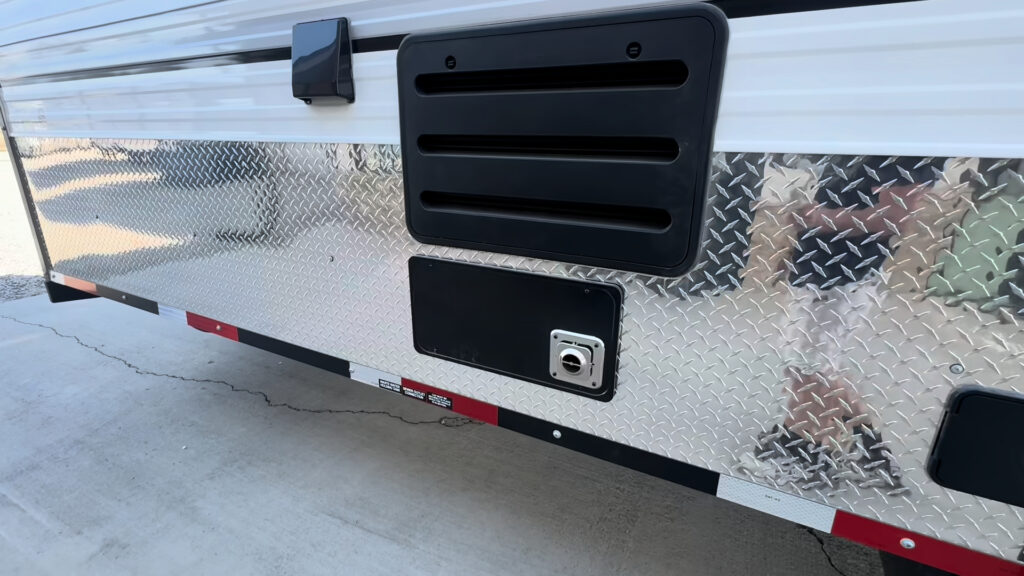 Close view of a black louvered vent and small access cover on the Kendall Camp lower sidewall.