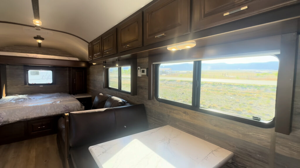 Interior view of the Kendall Camp dinette, side window, overhead cabinets, reclining sofa, and rear bed.