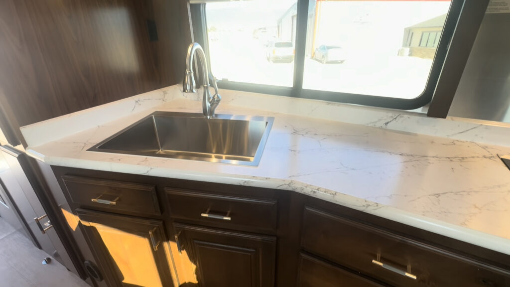 Close view of the Kendall Camp stainless steel kitchen sink, faucet, counter, window, and hardwood drawers.