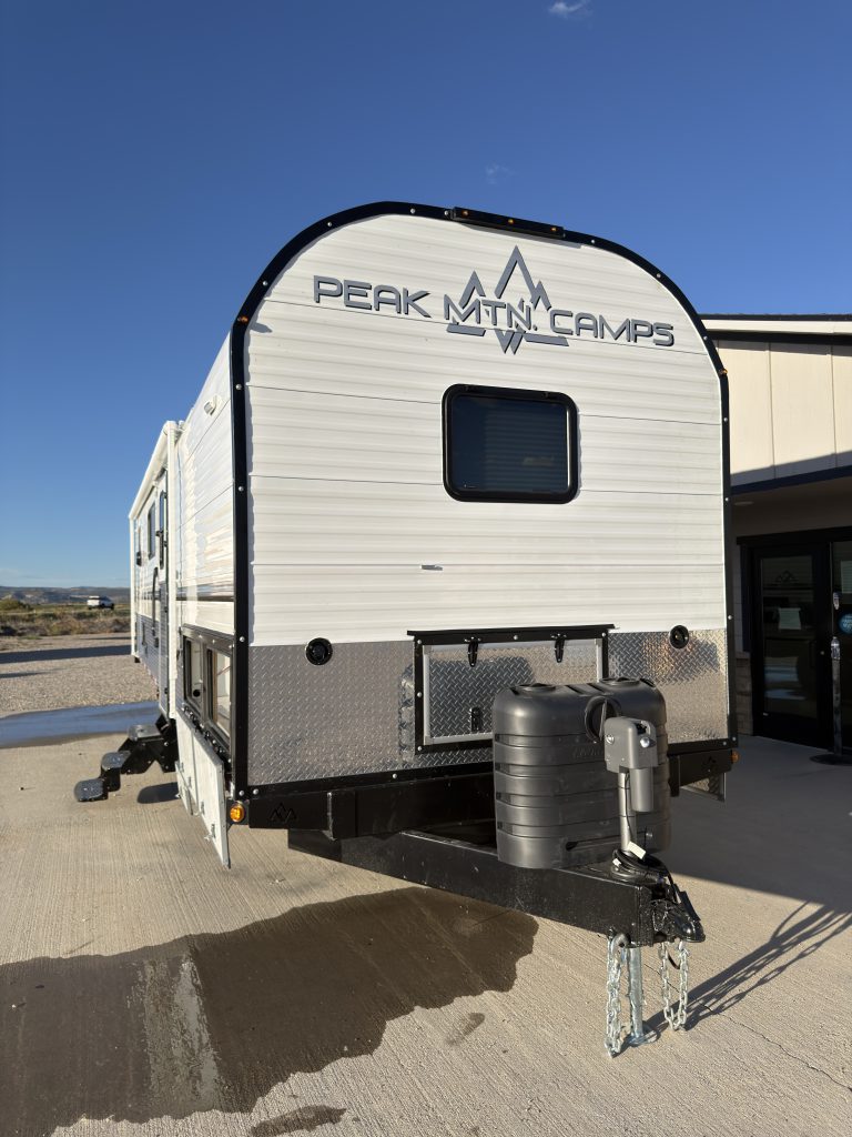 Front view with a window, Peak logo, covered propane cylinders, and towing hitch in Keulen Camp #132.