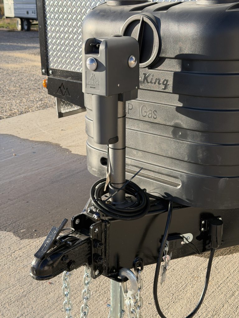 Close view of the hitch coupler, safety chains, and electric tongue jack in Keulen Camp #132.