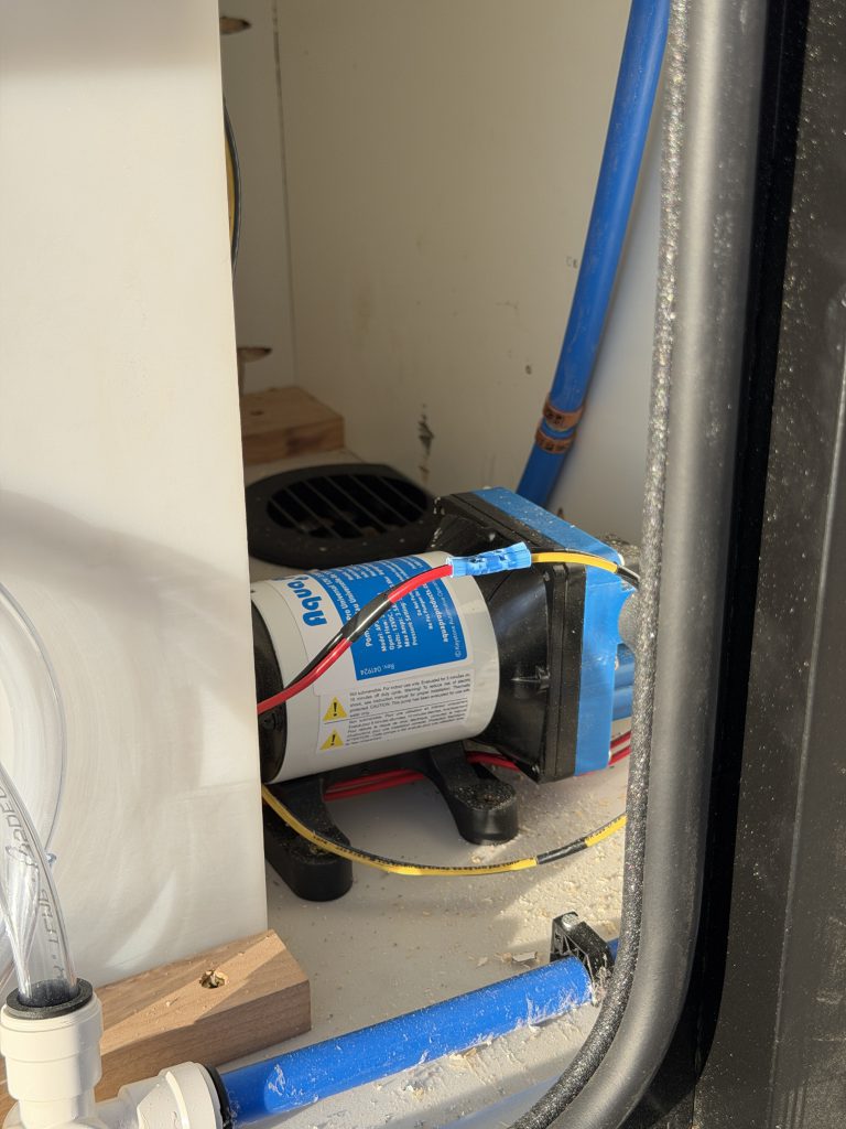 Close view of the water pump and connected plumbing inside the service compartment in Keulen Camp #132.