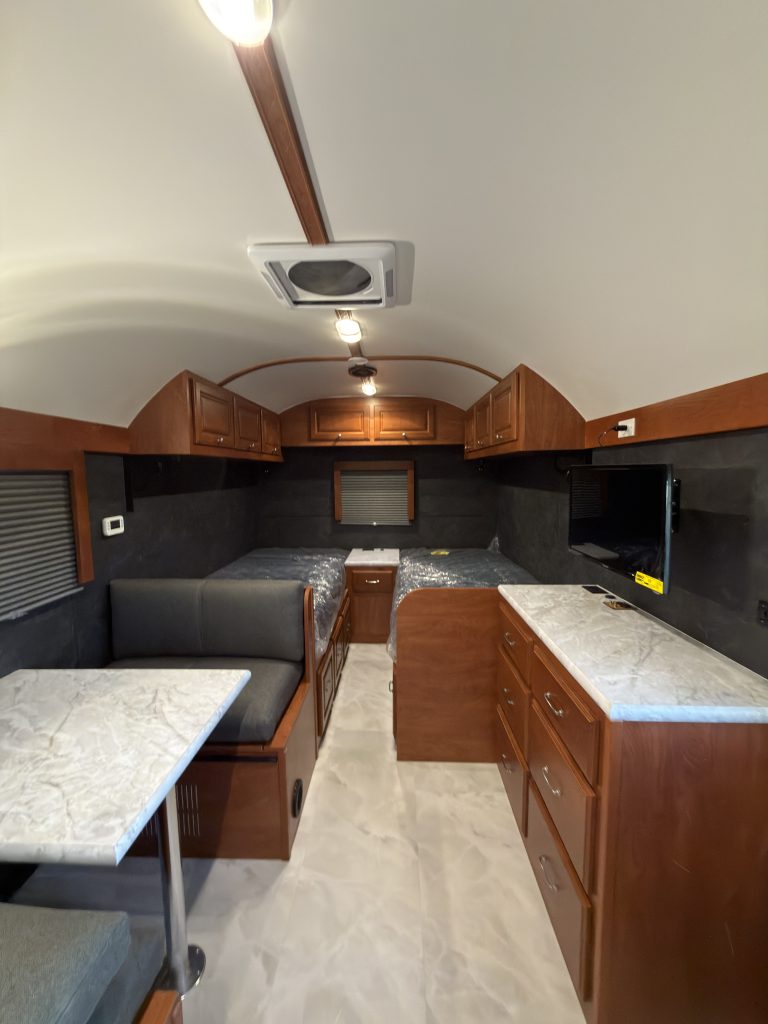 Twin mattress platforms, central nightstand, and living space beneath overhead cabinets in Keulen Camp #132.