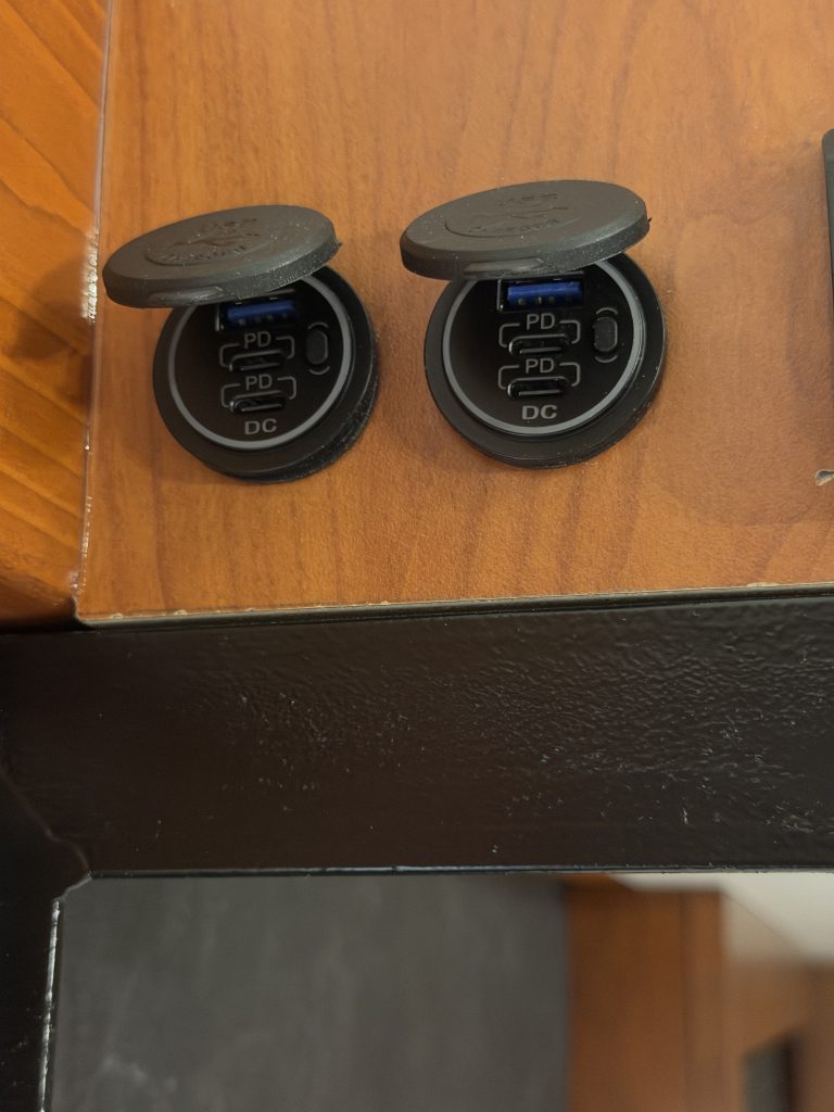 Two covered round charging outlets in wood trim near the entry and radio in Keulen Camp #132.