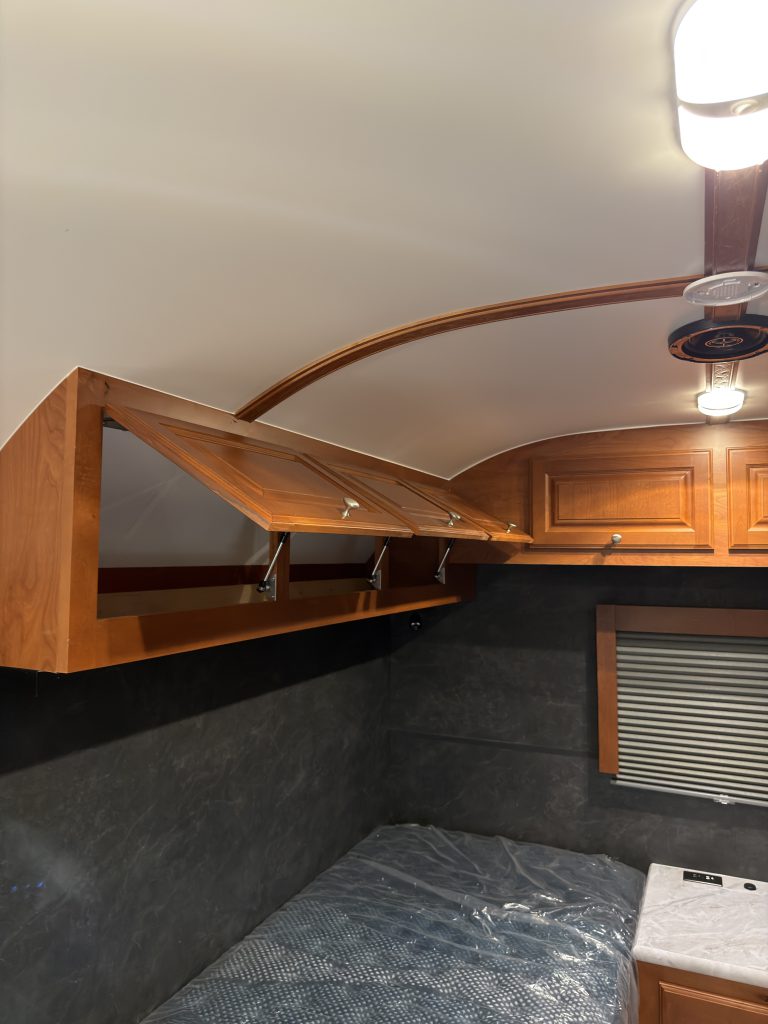Open overhead cabinets above a mattress platform in Keulen Camp #132.