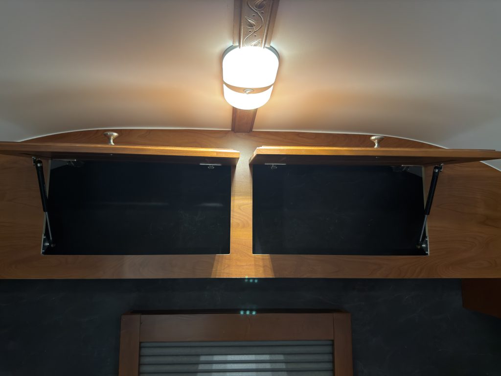 Open overhead storage on the front wall above the beds, beneath a ceiling light in Keulen Camp #132.