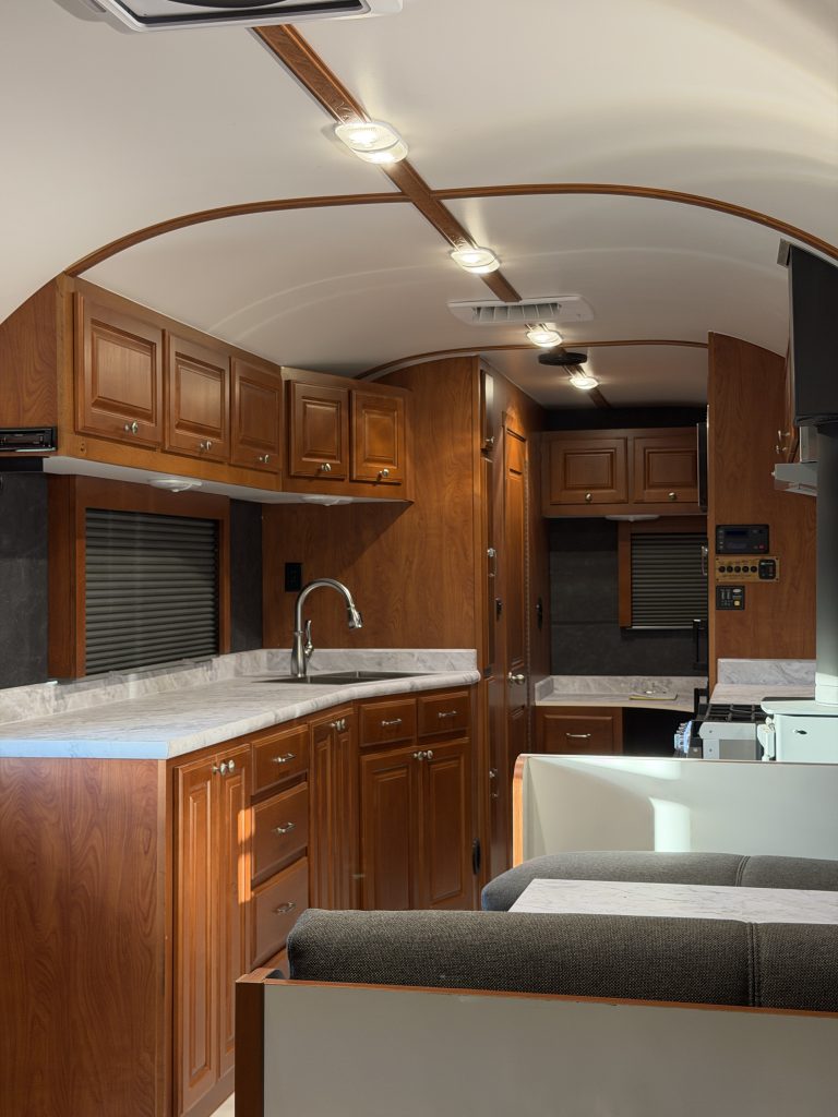 Closer view from the sleeping area along the interior aisle toward the kitchen cabinetry and cushioned seating in Keulen Camp #132.
