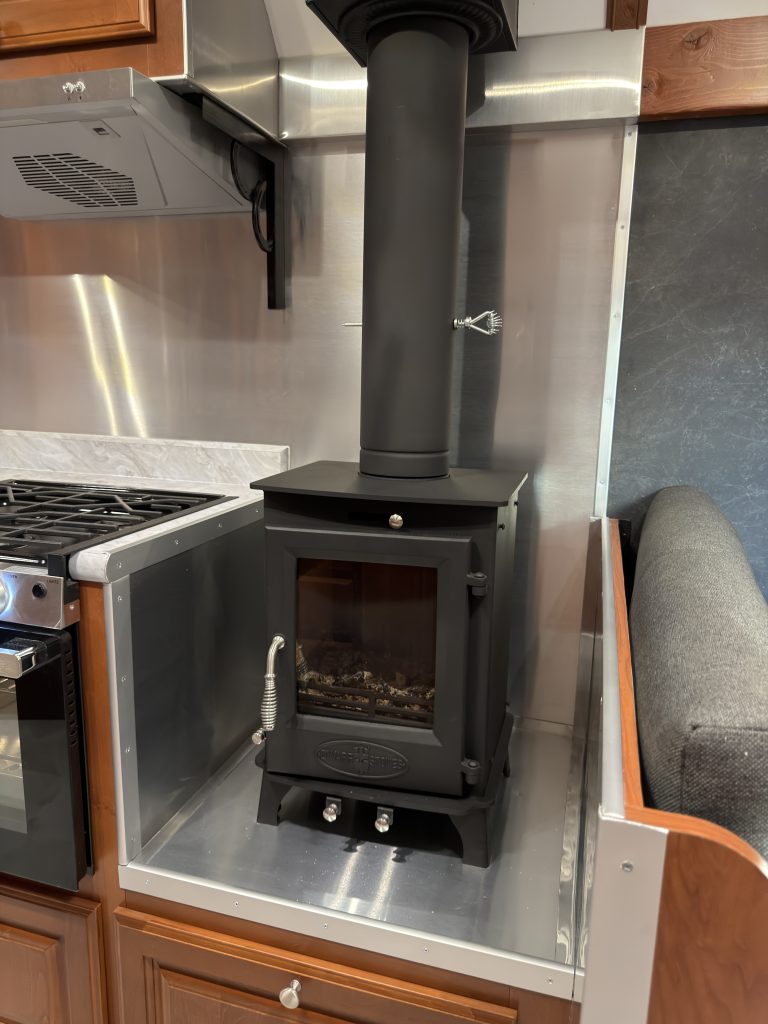 Small black wood stove with a tall flue and metal heat shielding in Keulen Camp #132.