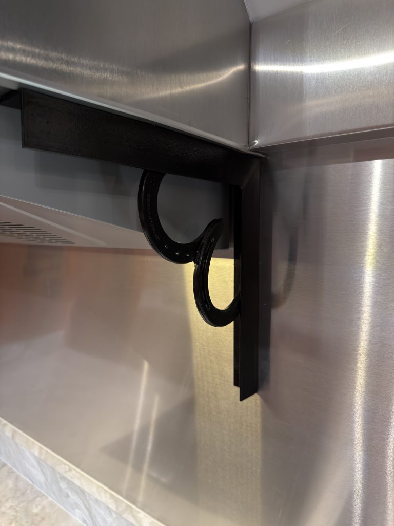 Welded horseshoe accents beside the stove flue and metal heat shielding in Keulen Camp #132.