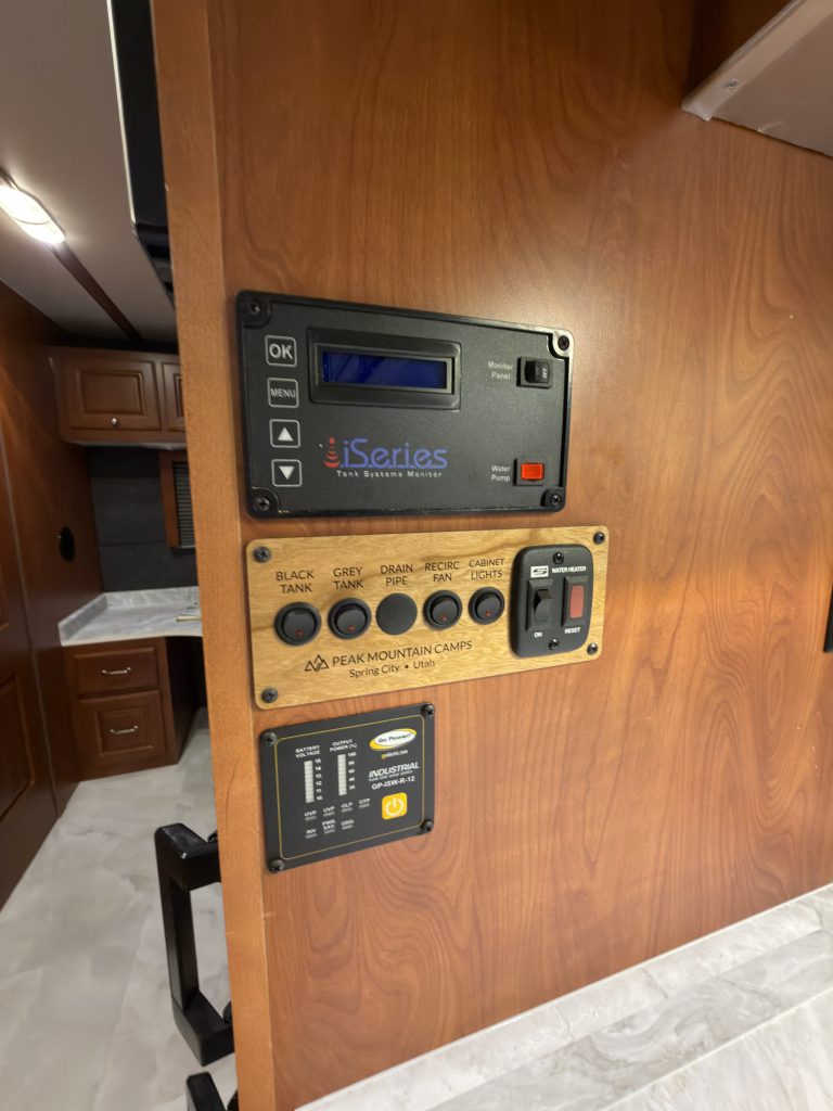 Inverter, tank, fan, and cabinet lighting switches and controls mounted in wood trim in Keulen Camp #132.