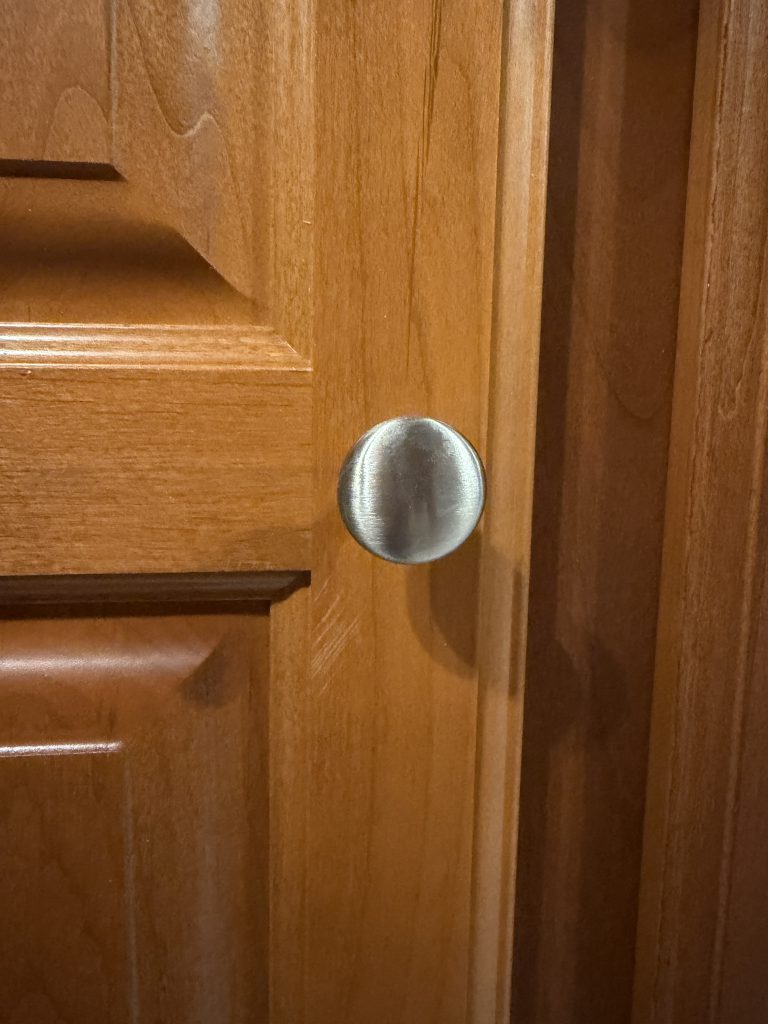 Round metal knob on a wood cabinet door in Keulen Camp #132.