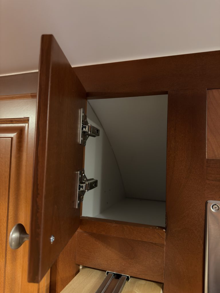 Empty upper cabinet with door open and hinges visible in Keulen Camp #132.