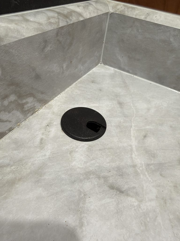Round black cable grommet set into the desk countertop in Keulen Camp #132.