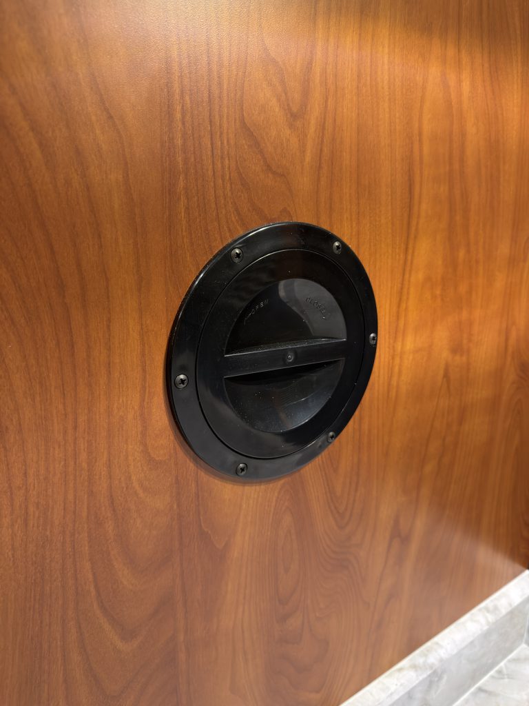 Round black shower plumbing access cover in wood cabinetry in Keulen Camp #132.