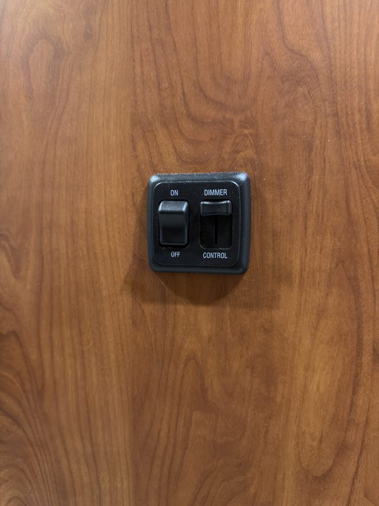 Two bathroom light switches mounted on wood paneling in Keulen Camp #132.