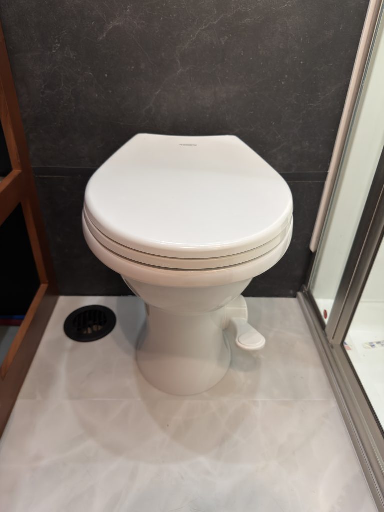 White toilet beside the shower base and floor vent in Keulen Camp #132.