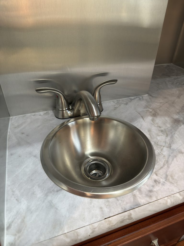 Round metal sink and faucet set into a stone-pattern countertop in Keulen Camp #132.