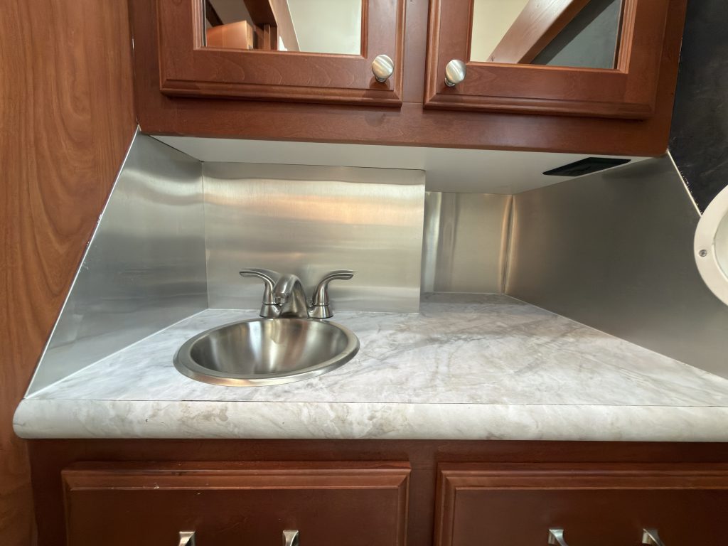 Bathroom sink beneath mirrored cabinets and metal backsplash in Keulen Camp #132.