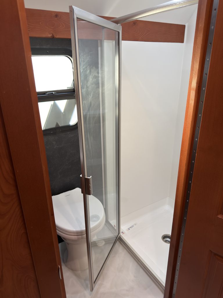 Glass shower door open beside the toilet in Keulen Camp #132.