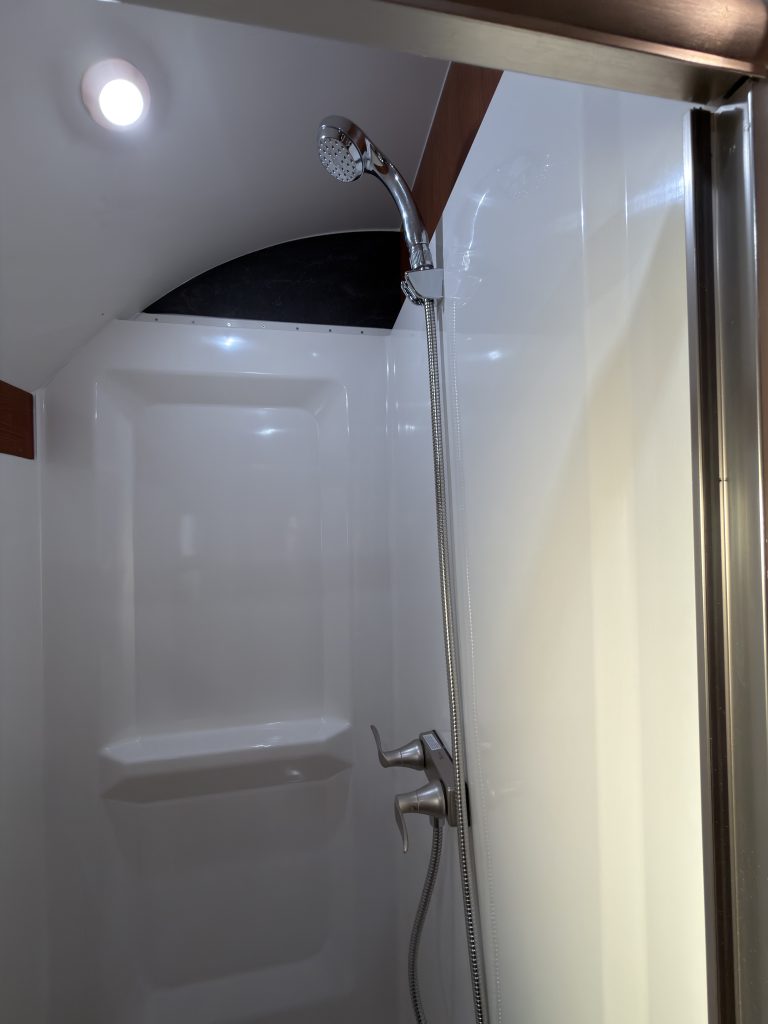 White shower enclosure with shower head and sloped ceiling in Keulen Camp #132.