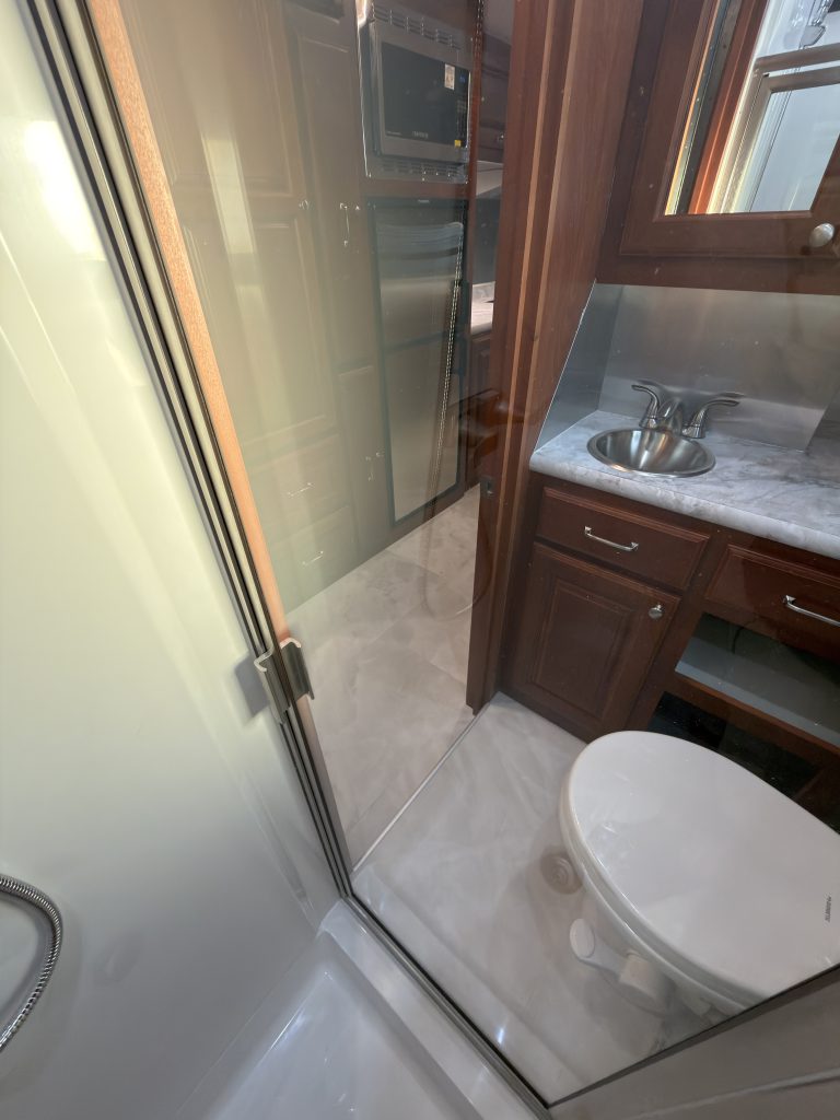 View through the glass shower enclosure toward the toilet and vanity in Keulen Camp #132.