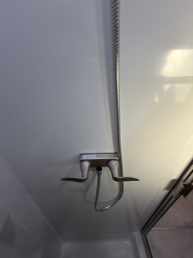 Shower mixer, hose, and white wall panel in Keulen Camp #132.