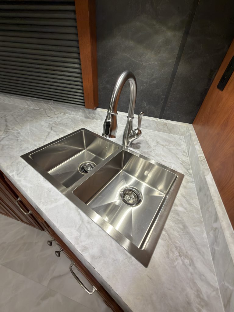 Double-bowl metal sink with tall faucet in a stone-pattern counter in Keulen Camp #132.
