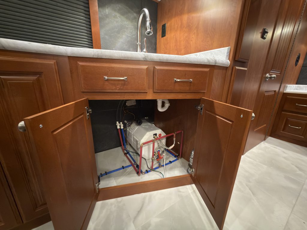 Open sink cabinet revealing plumbing and equipment in Keulen Camp #132.