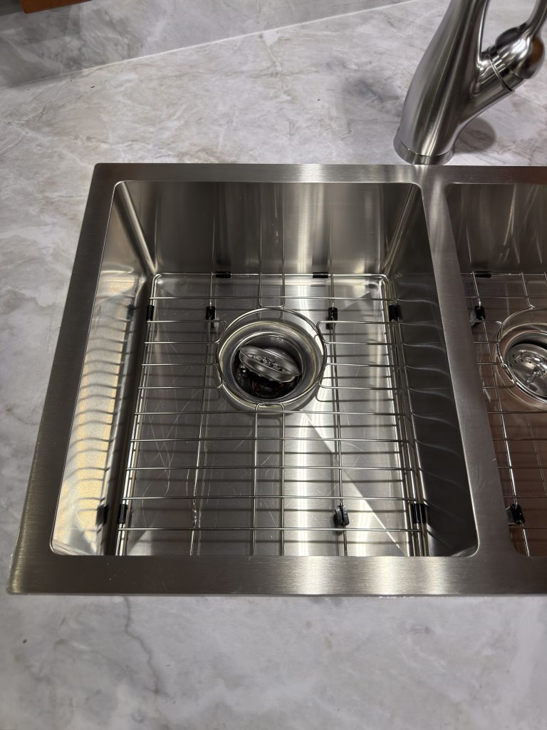 Close view of a metal sink basin, bottom grid, and drain in Keulen Camp #132.