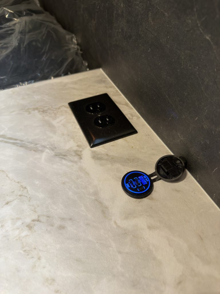 Nightstand power outlet and USB ports beside a mattress in Keulen Camp #132.