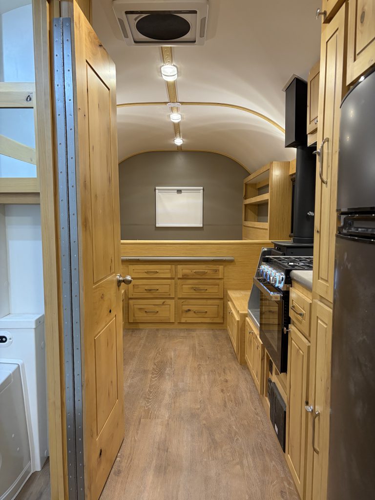 Van Niewkoop Camp #136: Interior aisle with hardwood cabinetry, luxury vinyl plank flooring, and the raised rear bed.