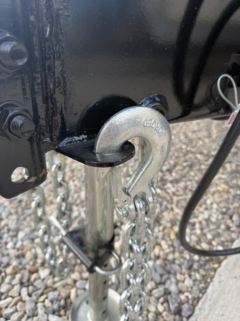 Close view of a metal safety-chain hook at the hitch in Van Niewkoop Camp #136.