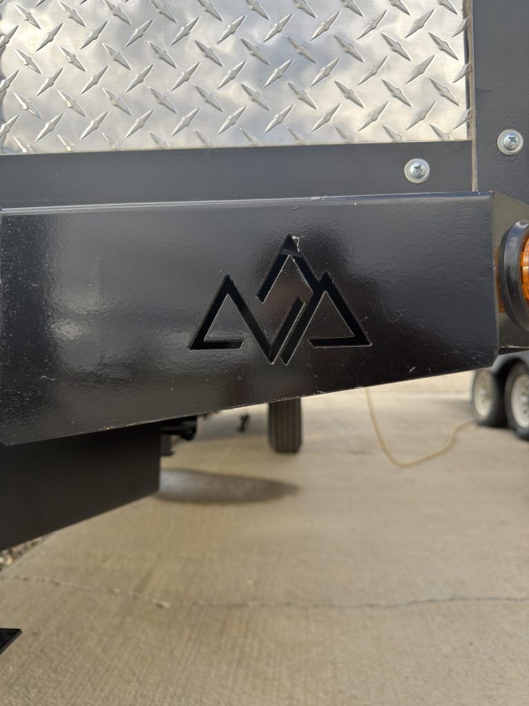 Van Niewkoop Camp #136: Black tongue frame plate with the Peak mountain logo beneath the diamond-plate wainscot.