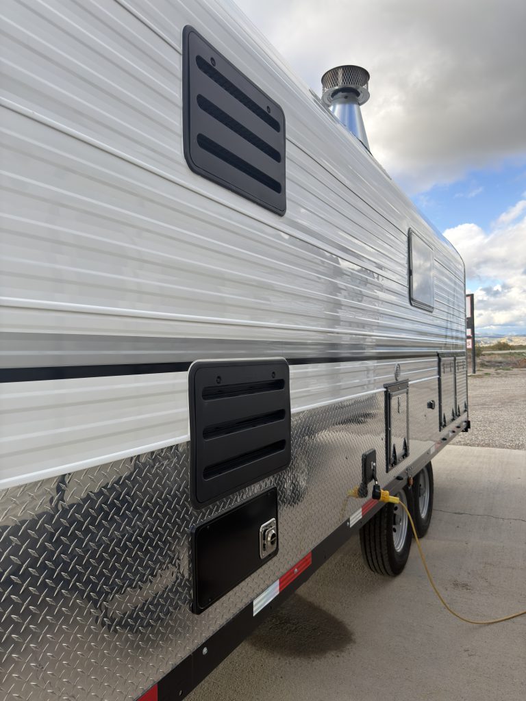 Van Niewkoop Camp #136: Roadside exterior with refrigerator vents, a furnace vent, and tandem trailer axles.