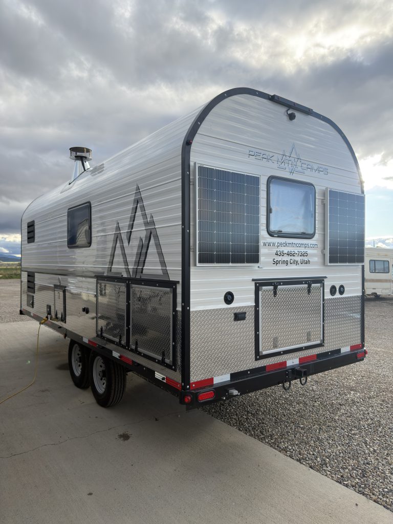 Van Niewkoop Camp #136: Angled rear view with two solar panels, the rear window, and roadside storage doors.