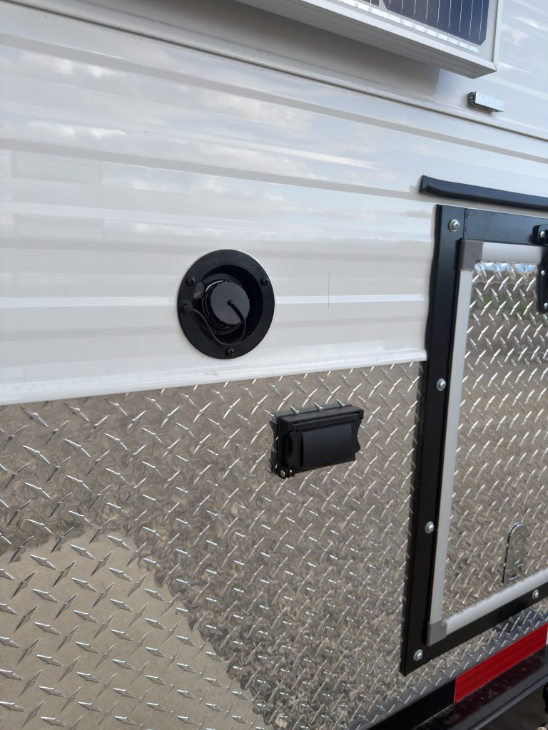 Van Niewkoop Camp #136: Rectangular exterior AC outlet below a round service port beside the storage hatch.