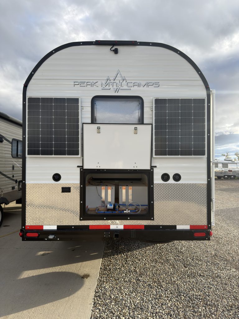 Van Niewkoop Camp #136: Rear exterior with the water-system storage hatch raised beneath the window and solar panels.