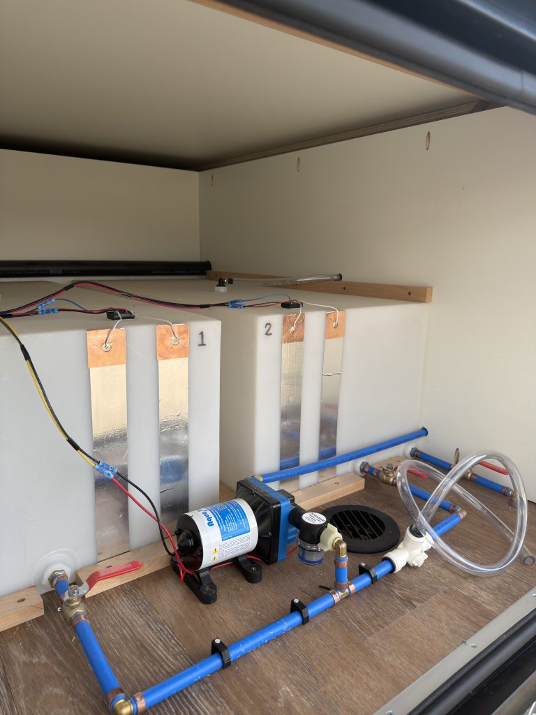 Van Niewkoop Camp #136: Rear compartment showing the Shurflo pump, tubing, and accessible plumbing connections.