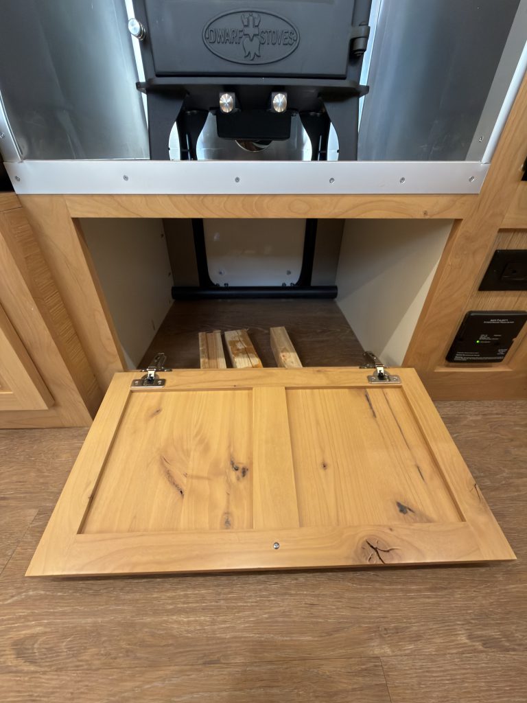 Van Niewkoop Camp #136: Interior access to the pass-through wood box beneath the wood stove, with its panel lowered.