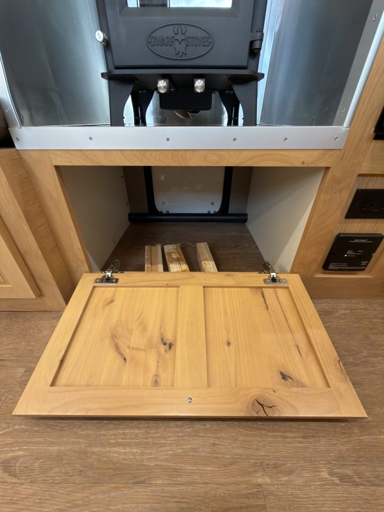 Van Niewkoop Camp #136: Pass-through wood box beneath the wood stove with the interior access panel folded down.