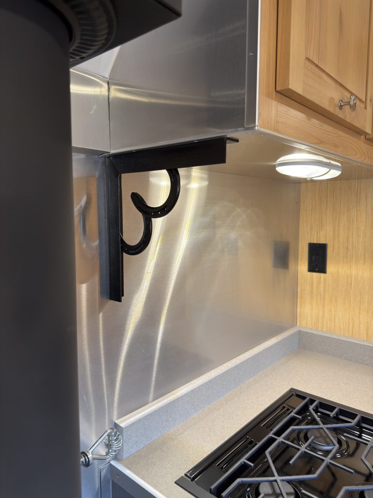 Van Niewkoop Camp #136: Horseshoe accent bracket beneath the upper kitchen cabinet beside the LED light and metal backsplash.