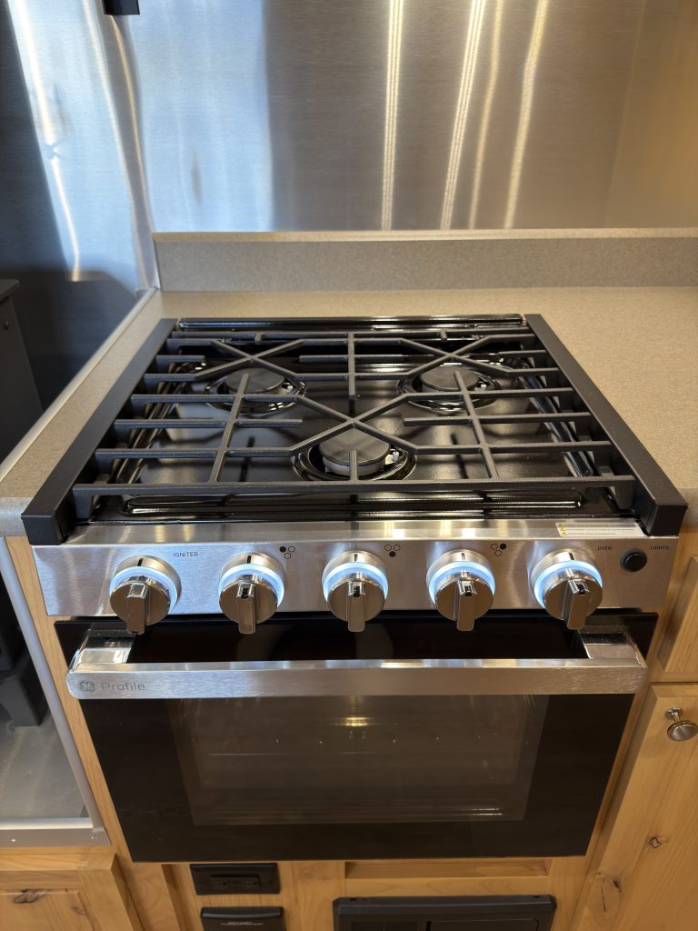 Van Niewkoop Camp #136: Three-burner GE cooktop and oven in front of the metal backsplash.