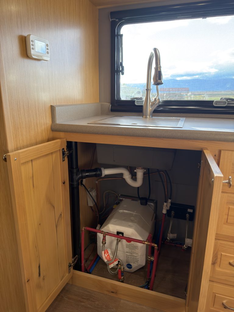 Van Niewkoop Camp #136: Open sink base cabinet showing accessible plumbing and equipment beneath the basin.